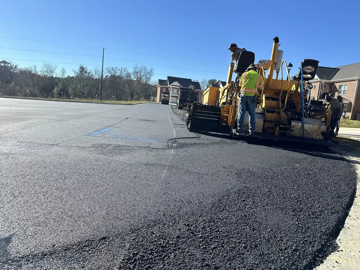 Paving crew laying a fresh mat of hot mix asphalt behind a paver on a commercial lot