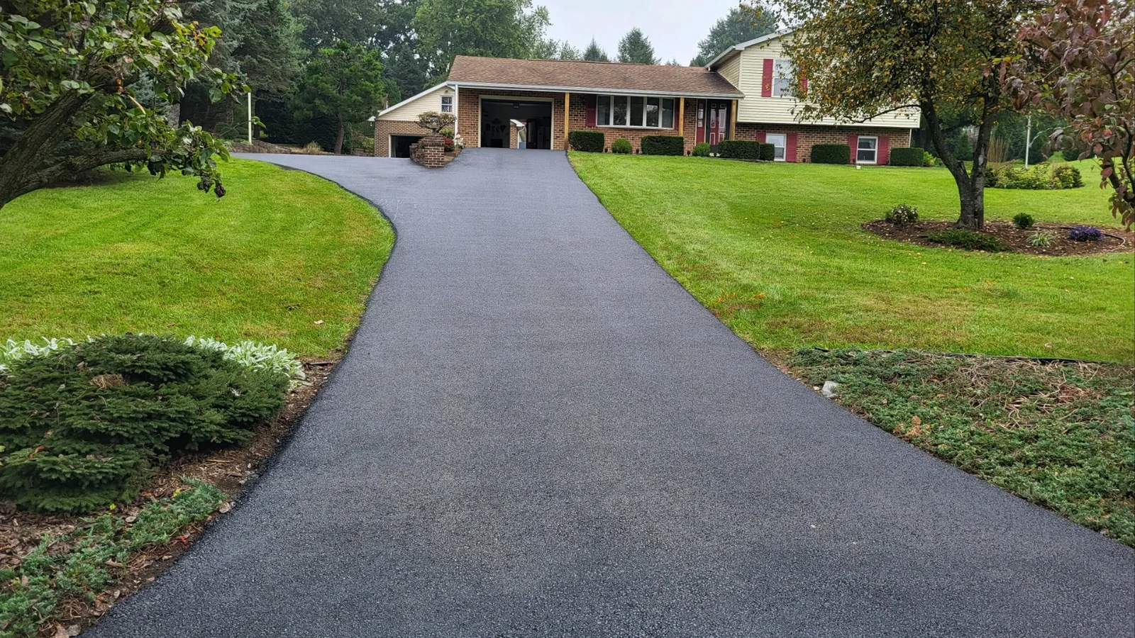 Long new asphalt driveway climbing to a brick ranch house across a green lawn