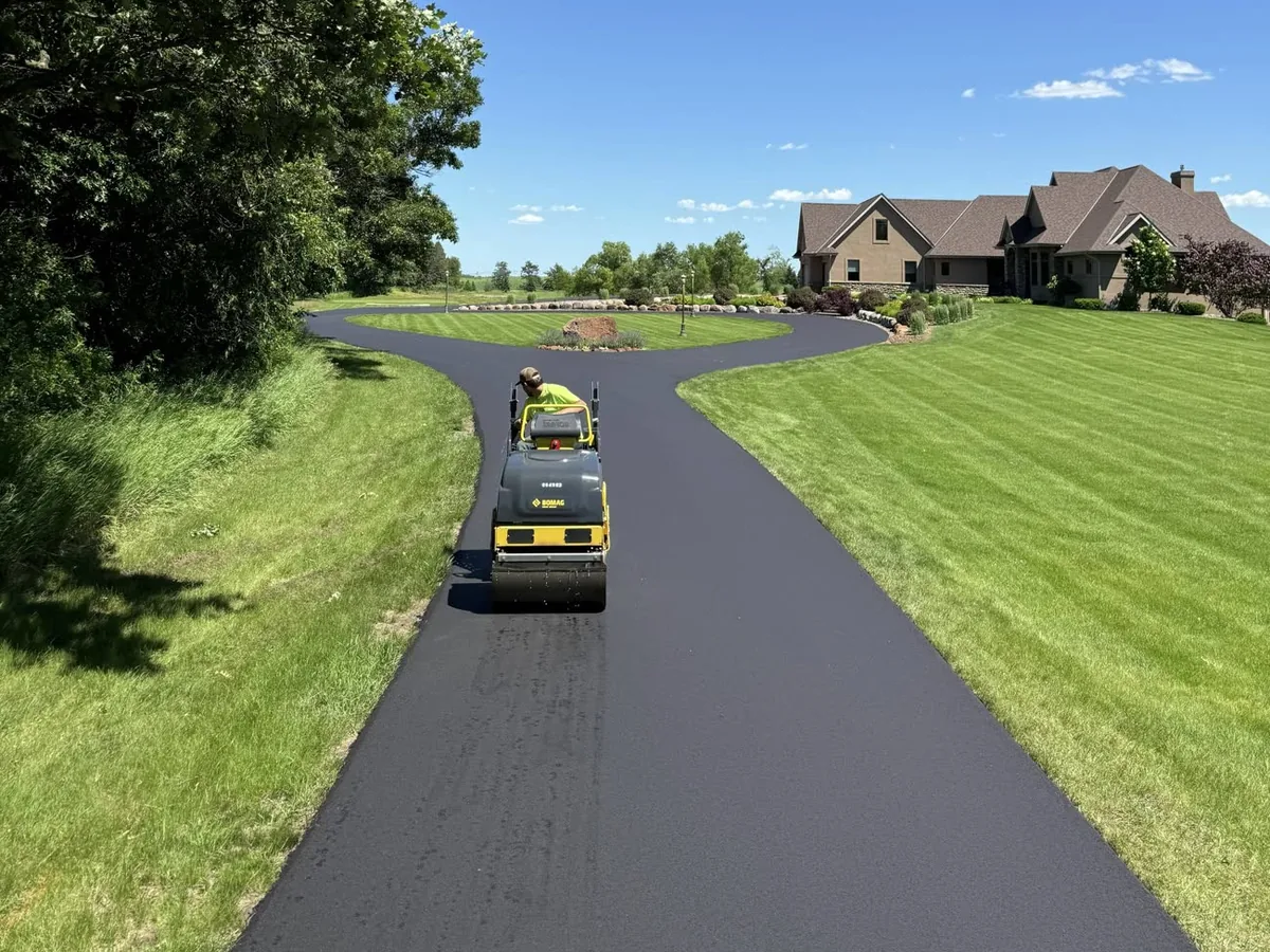 Roller compacting a freshly paved asphalt driveway beside a green lawn