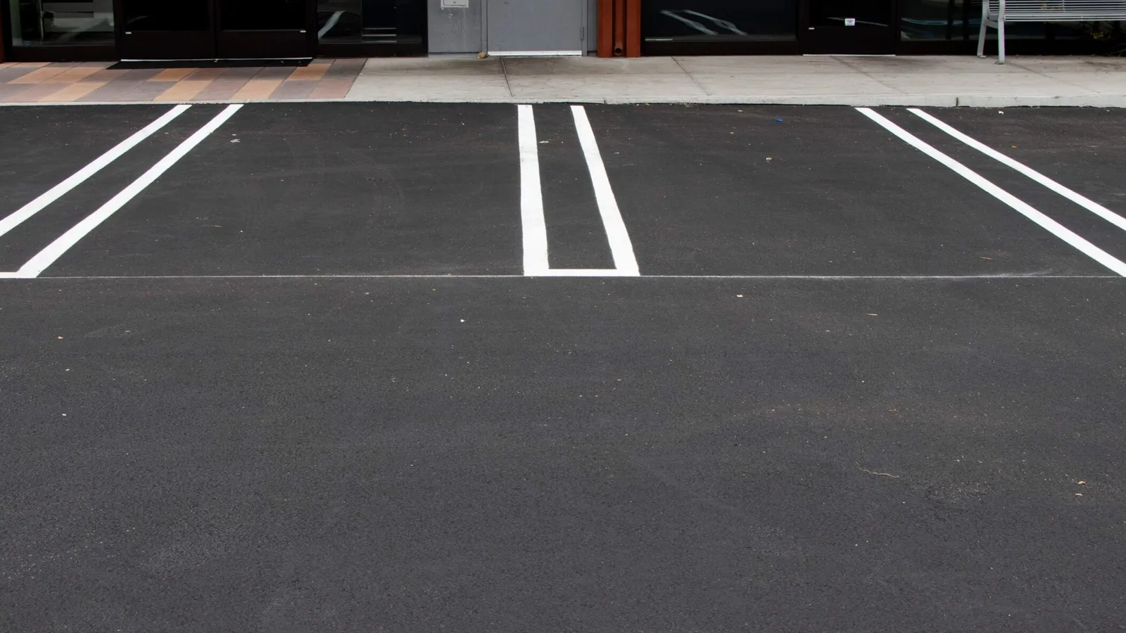 Fresh white parking stalls striped on new asphalt in front of a retail entrance