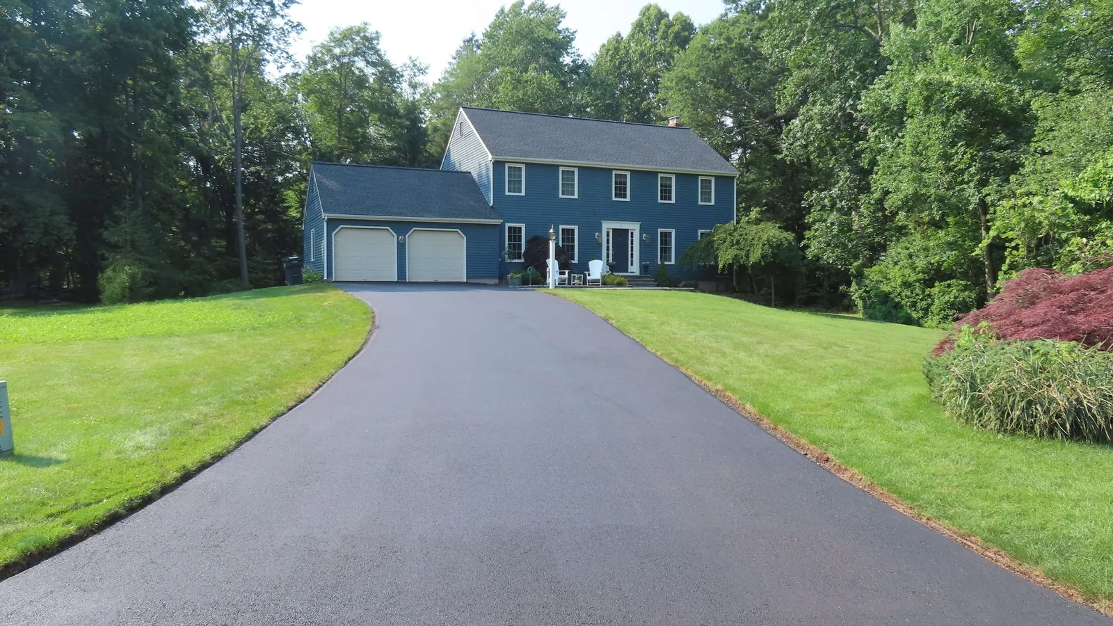 Long fresh asphalt driveway running through the woods to a house