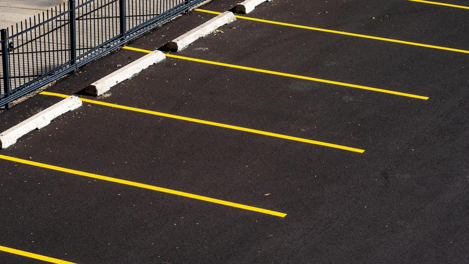 Fresh yellow stall lines painted on a newly paved asphalt lot with concrete wheel stops