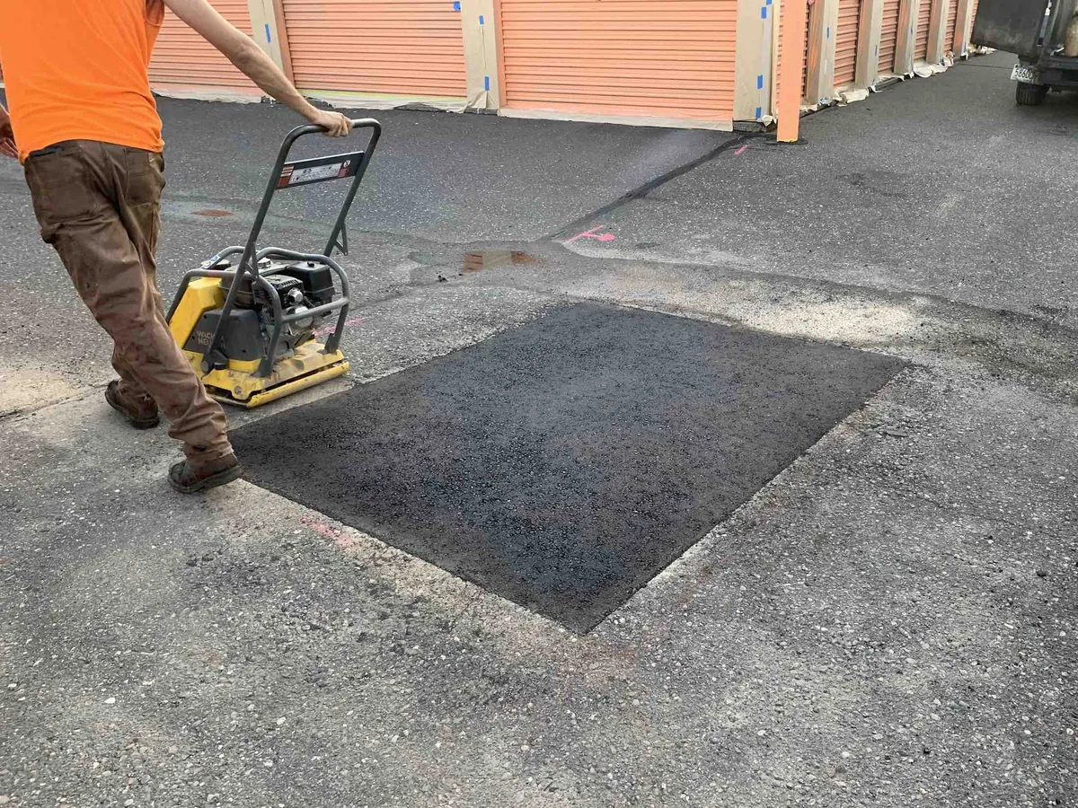 Plate compactor packing down a fresh hot mix patch in an asphalt drive lane