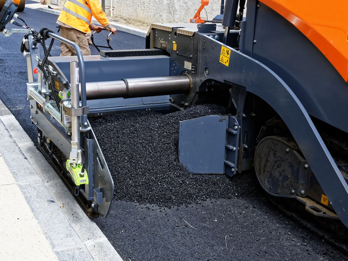 Paver screed laying a new black asphalt lift against the curb over the old surface