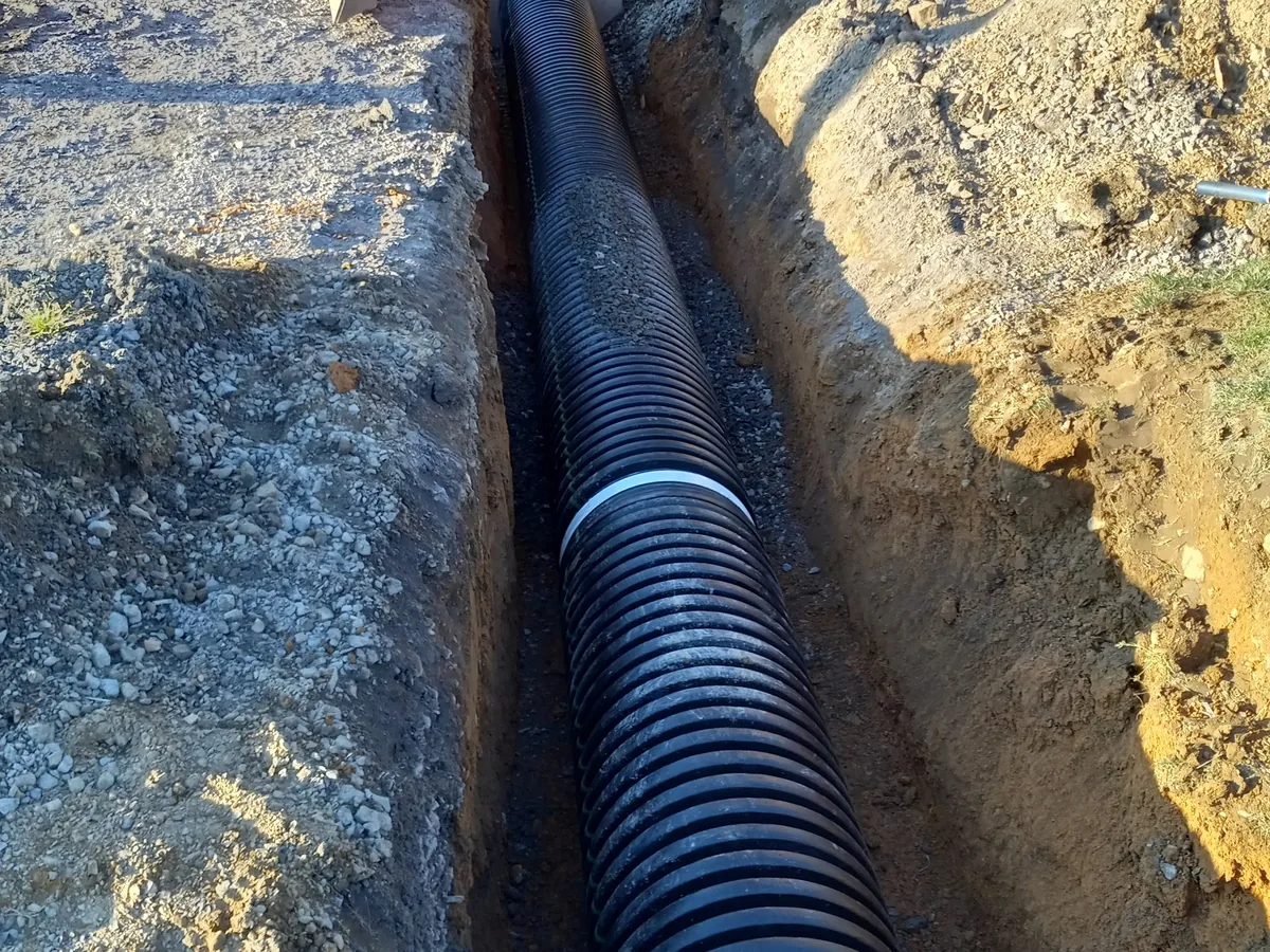 Drainage pipe bedded in a gravel trench along a driveway
