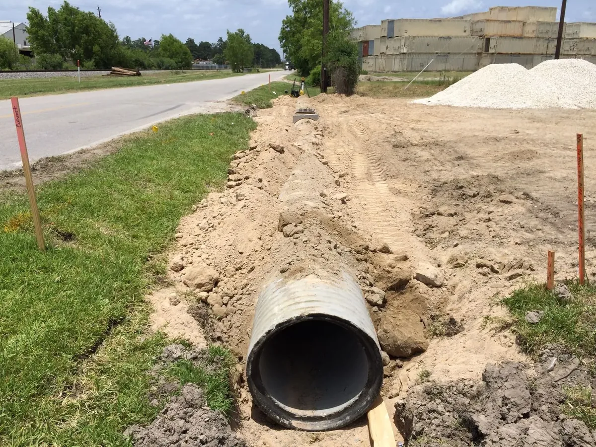 Culvert pipe set in a trench at a driveway entrance with sandy spoil alongside