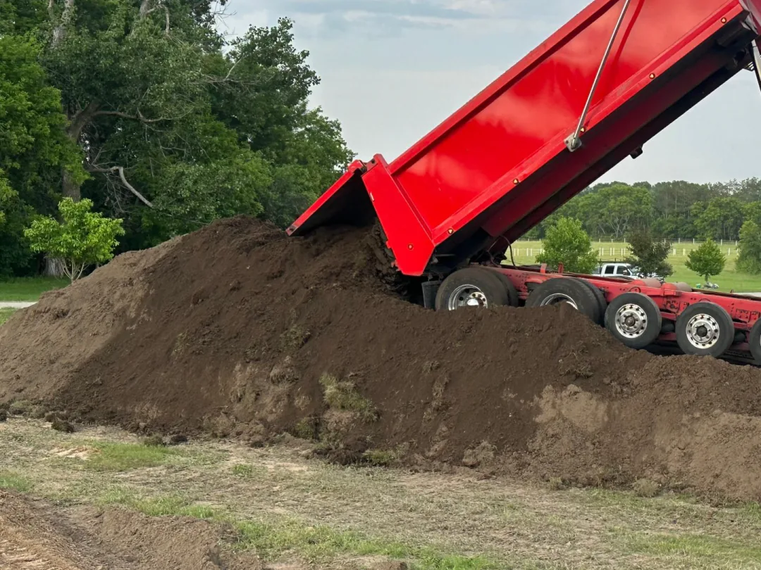 Dump truck tipping a load of fill dirt onto a graded yard