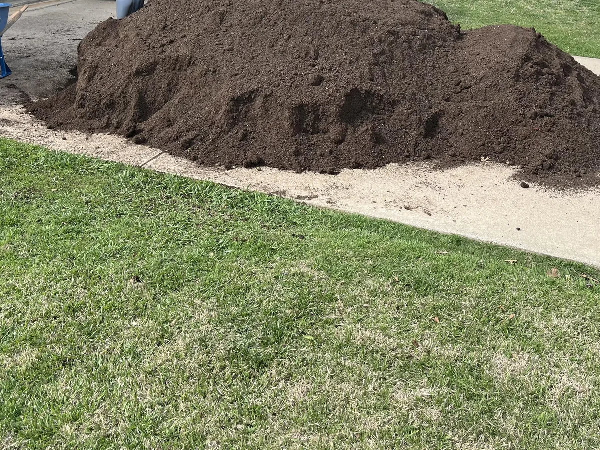 Pile of dark topsoil dropped on a driveway with a wheelbarrow beside it