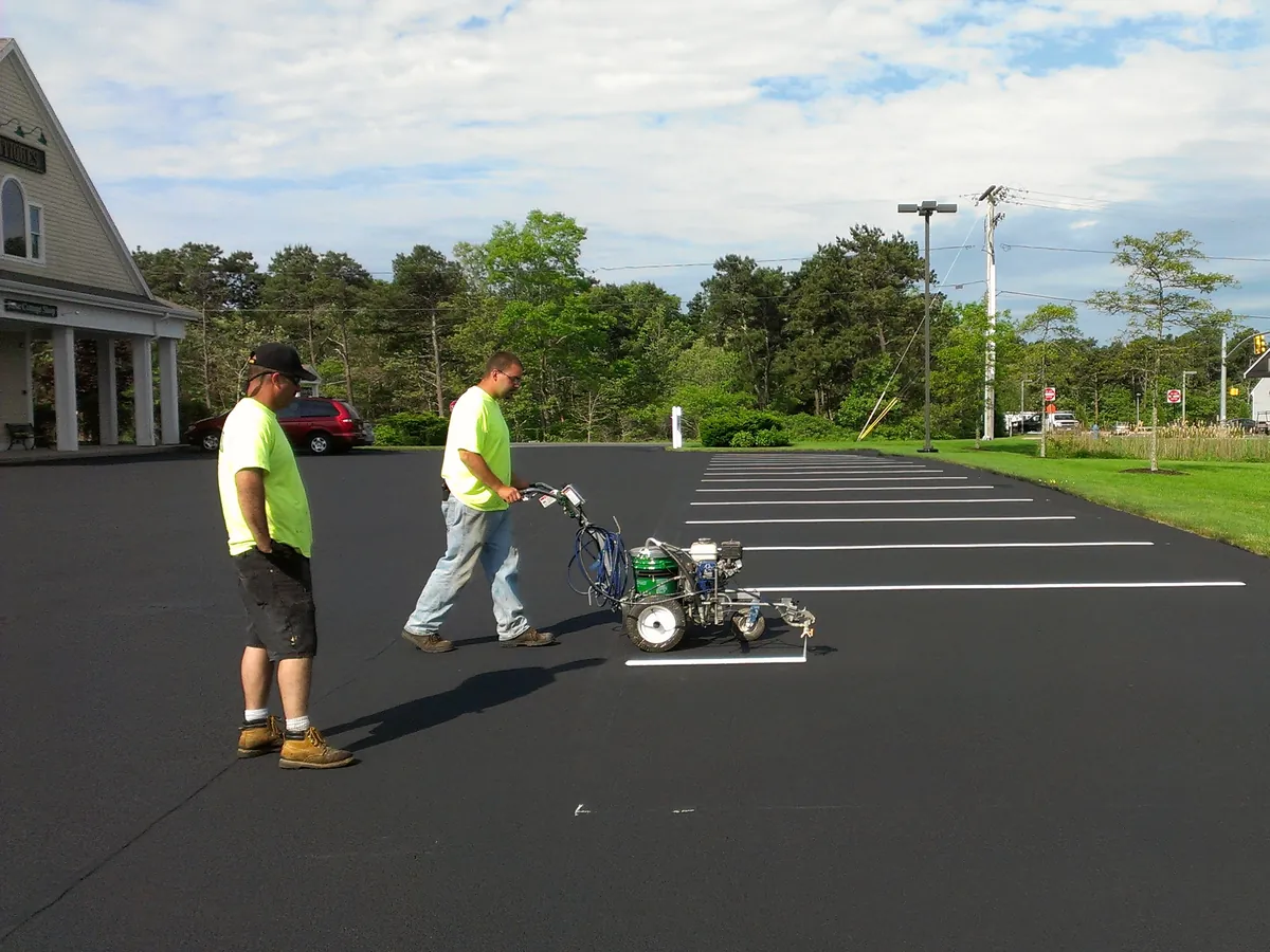 Two workers restriping parking stalls on a freshly sealed asphalt lot