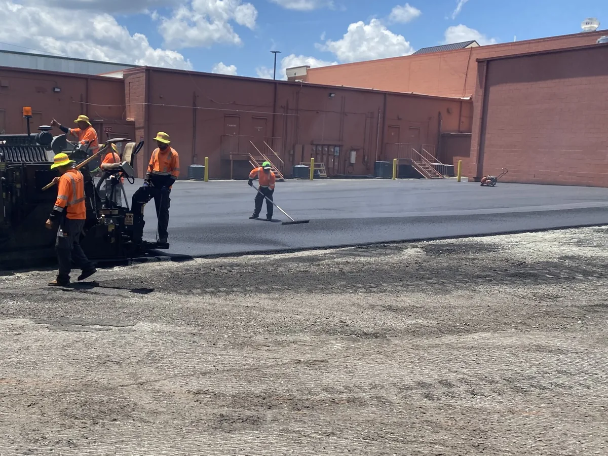 Paving crew laying a new asphalt surface across a commercial parking lot