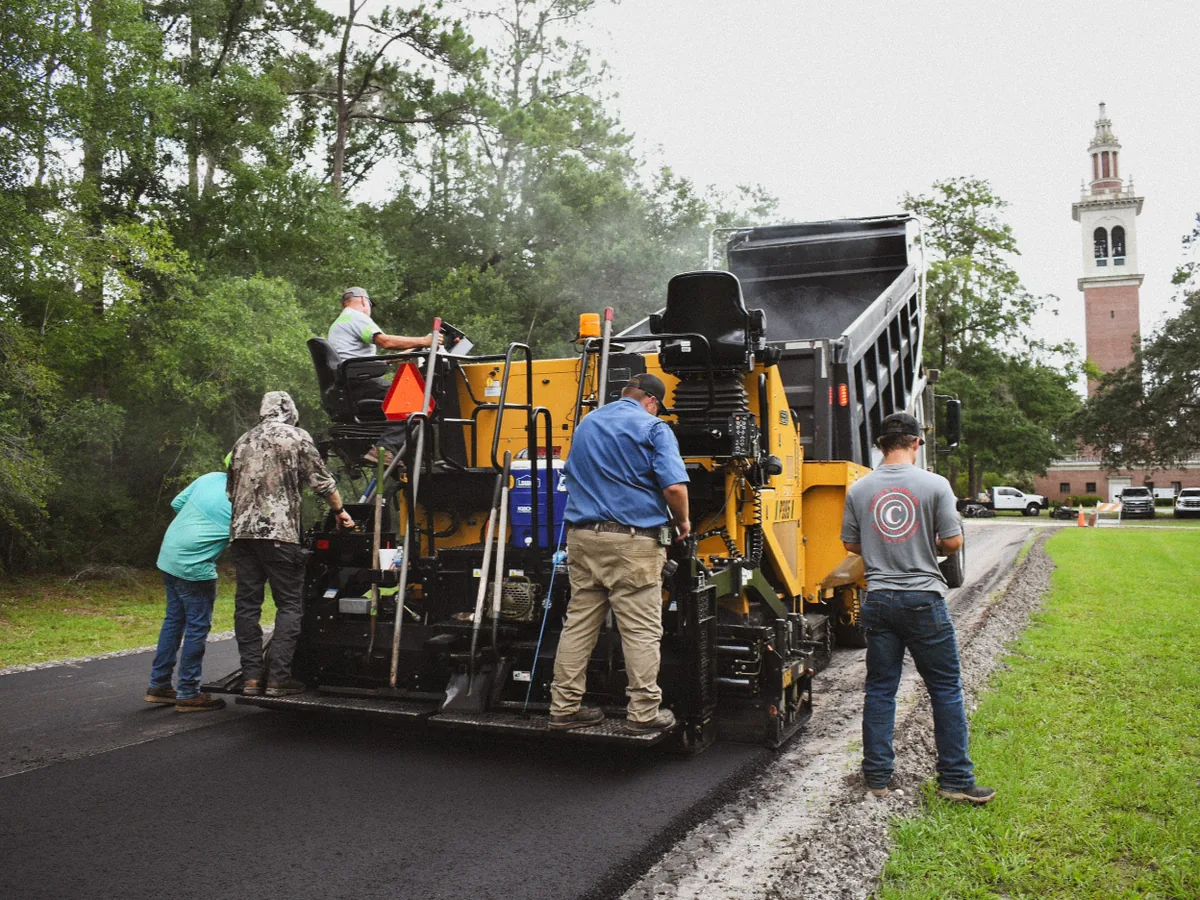 Crew paving a new asphalt drive with a paver and haul truck