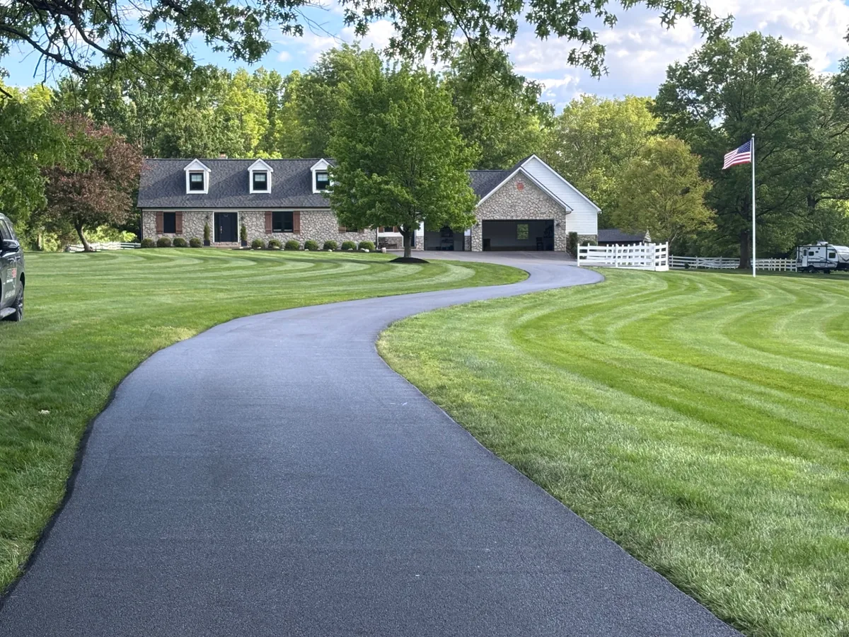 Freshly sealcoated asphalt driveway curving across a mowed lawn to a house