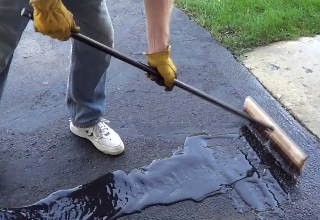 Worker spreading black sealer across asphalt with a squeegee